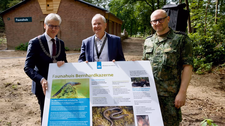  3 mannen voor een Faunahuisje. Ze houden groot bord vast met informatie over Faunahuis Bernhardkazerne.    