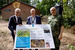 3 mannen voor een Faunahuis. In hun handen een groot bord met informatie over het Faunahuis op de Bernhardkazerne