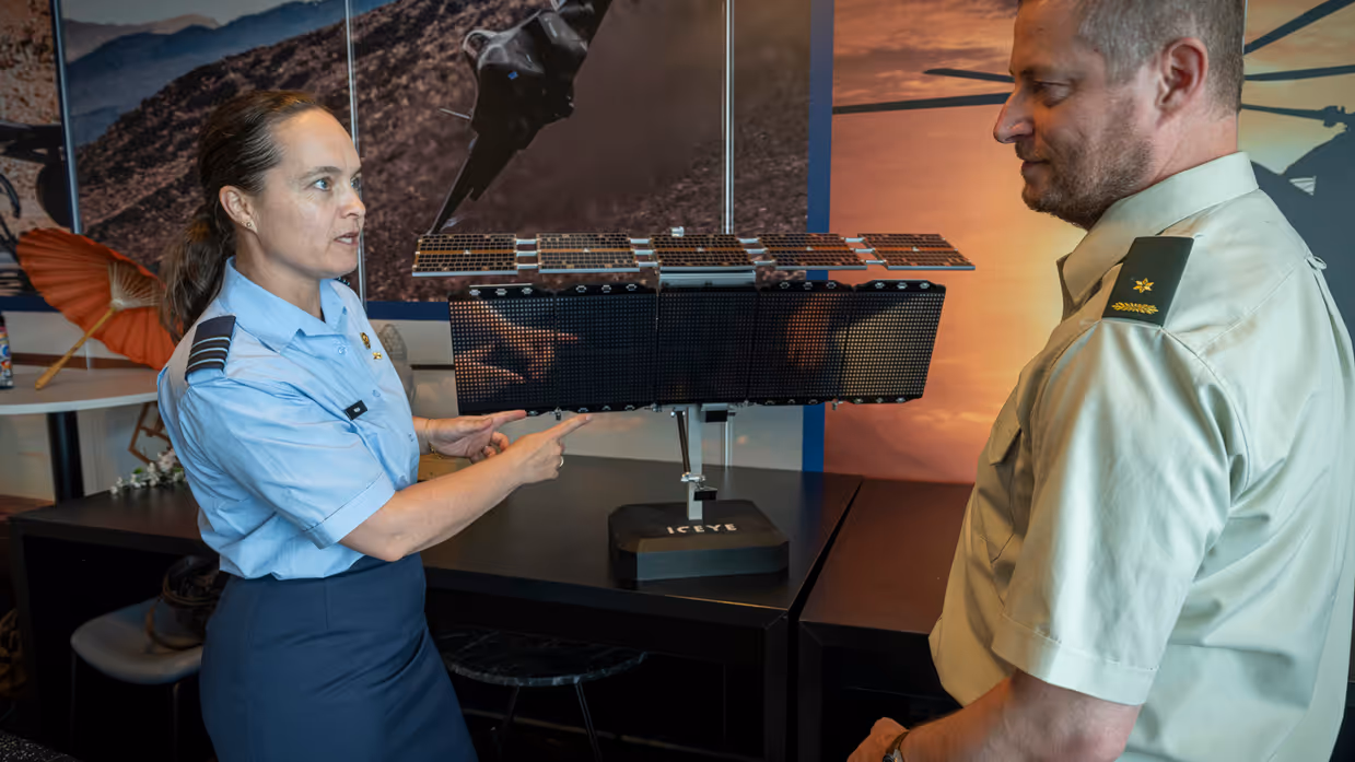 Luitenant-kolonel Petra Wijnja in gesprek met liaison-officer van de landmacht bij een model van een SAR-satelliet van het Finse ICEYE
