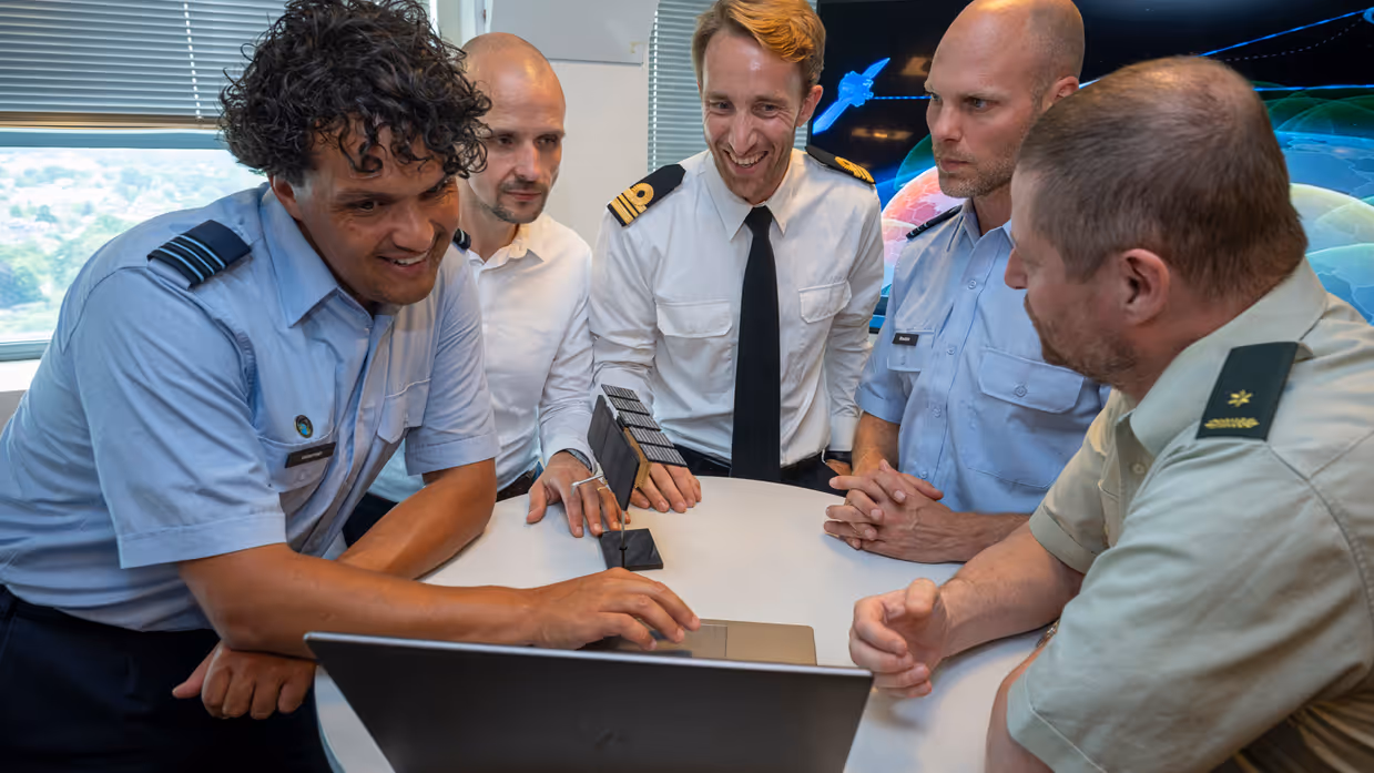 Groepsfoto van enkele militairen en burgers met in een midden een model van een satelliet.