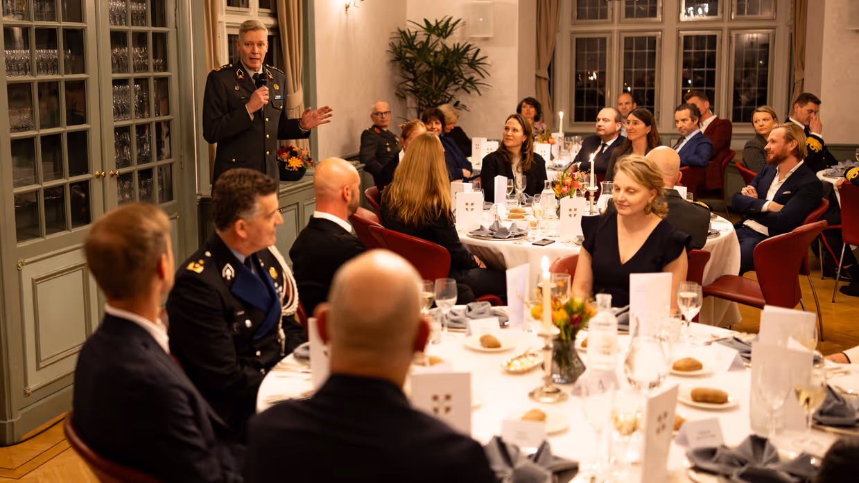 Generaal Maas spreekt de aanwezigen toe in een volle zaal.