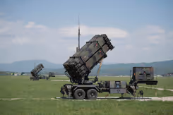 2 Patriot-luchtverdedigingssystemen op grasland met heuvellandschap op de achtergrond.