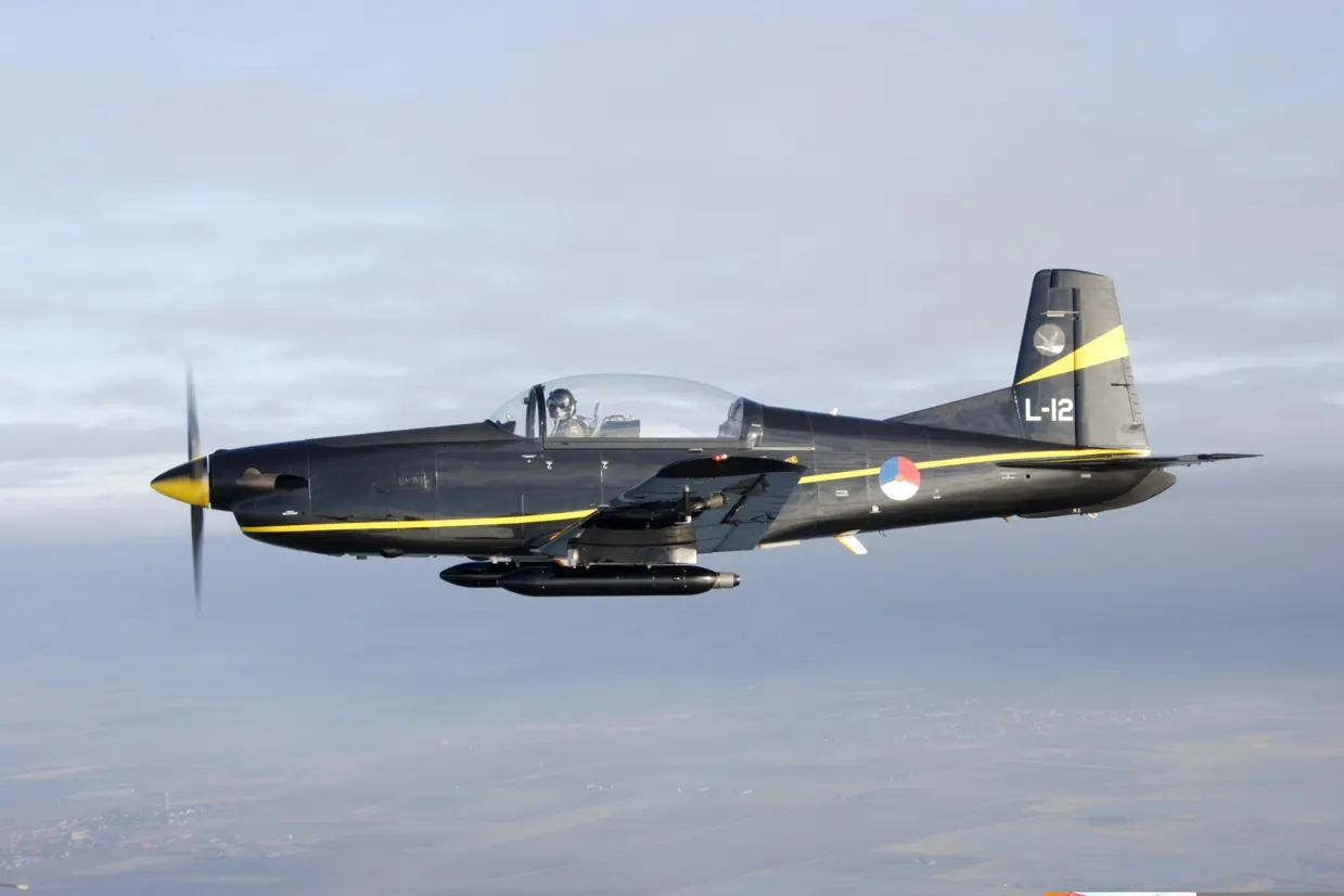 Zijaanzicht van PC-7 lesvliegtuig in de lucht.