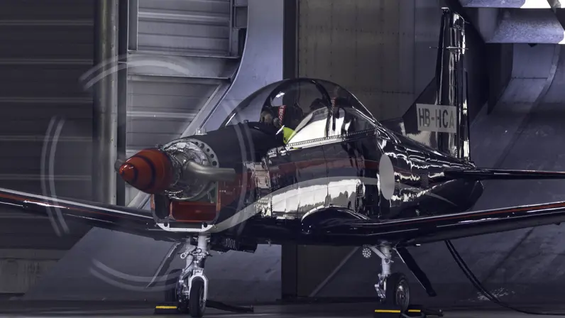 Een PC-7 MKX-lesvliegtuig met draaide propeller in een hangaar.