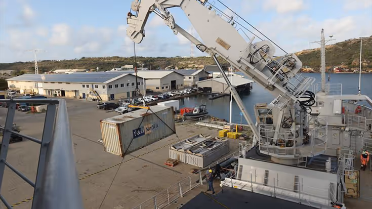 Een container hangt in de kraan van Zr.Ms. Pelikaan boven een kade