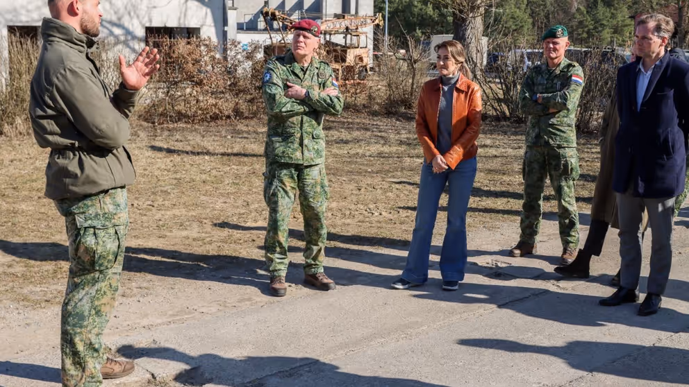 De minister en enkele militairen luisteren naar een andere militair.