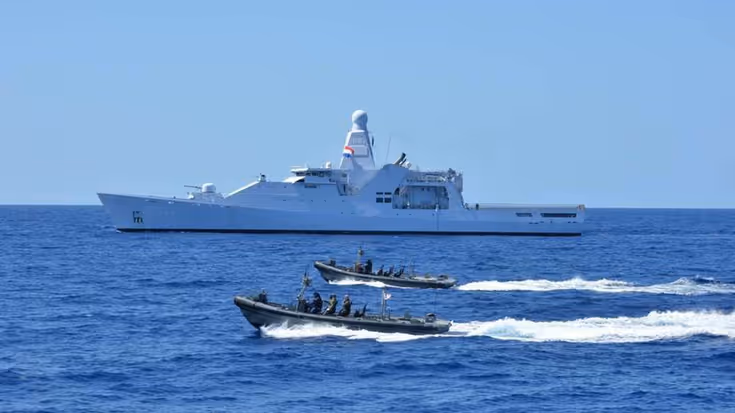 Een marineschip op zee, geflankeerd door snelle onderscheppingsboten.