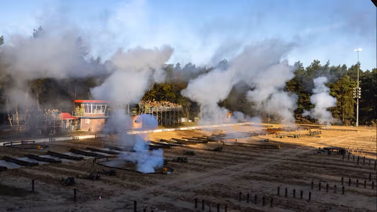 Militairen tijgeren door het zand. Om hen heen zijn rookpluimen.