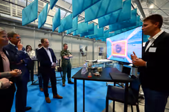 7 mensen in bij een tafeltje en groot scherm. Een man legt iets uit. 