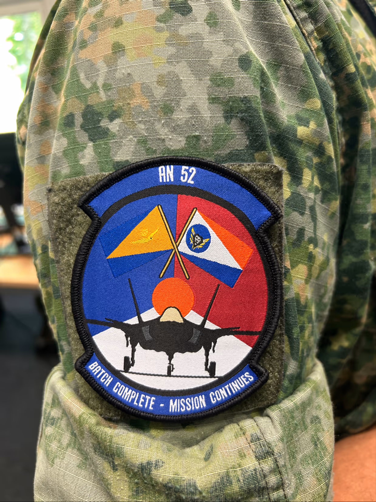 Mouw met daarop een badge met de tekst ‘AN 52; Badge complete - mission continues’.