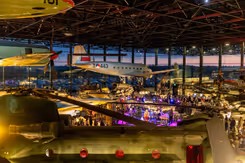 Bovenaanzicht van museumvloer met vliegtuigen die aan het plafond zijn bevestigd en mensen eronder.