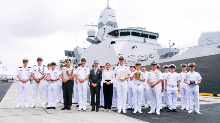 De ministers staan op een kade tussen Japanse mariniers, met daarachter het schip.