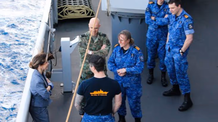 De minister praat met militairen aan boord van een schip.