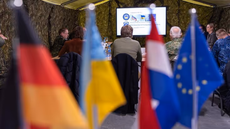 Vlaggetjes van Duitsland, Nederland, Europa en Oekraïne op een bureau in een legertent.