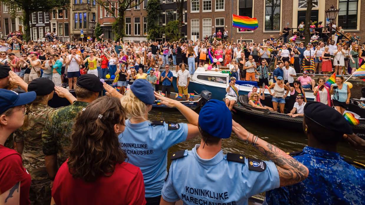 Militairen salueren vanaf de gracht naar het publiek aan de kant.