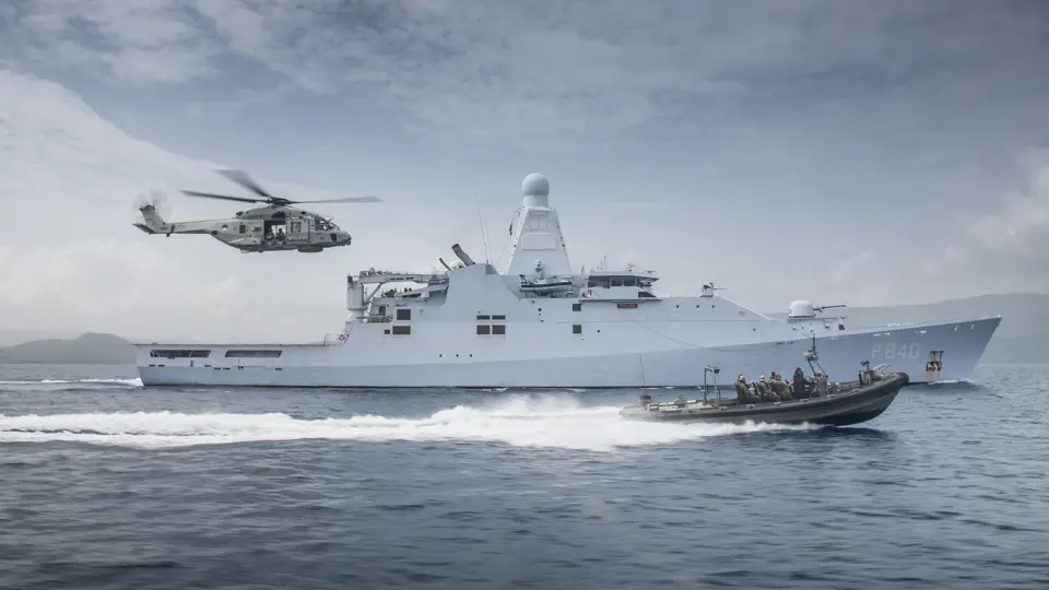 Schip op zee met boot die er naast vaart en een helikopter volgt.