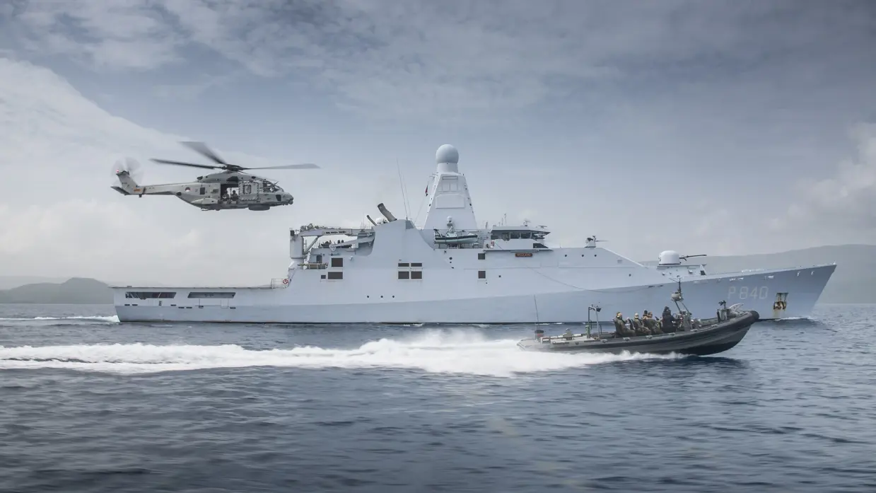 Schip op zee met boot die er naast vaart en een helikopter volgt.