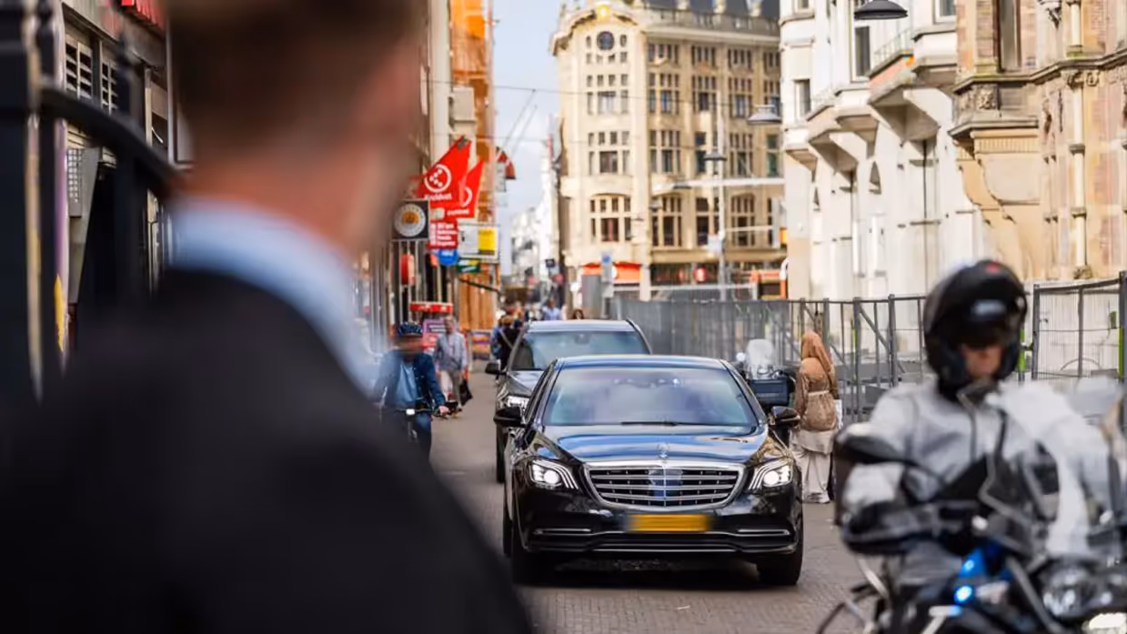 Een beveiliger op de voorgrond kijkt naar aankomende auto’s in de binnenstad.