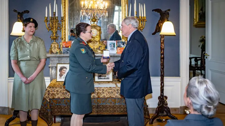 Militair overhandigt nabestaande onderscheiding.