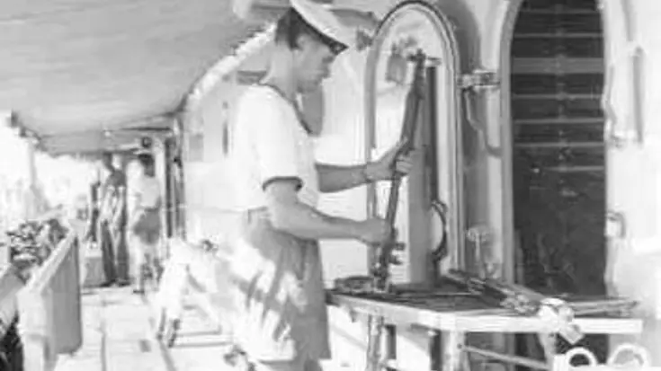 Marineman maakt geweer schoon aan boord van schip (1955).