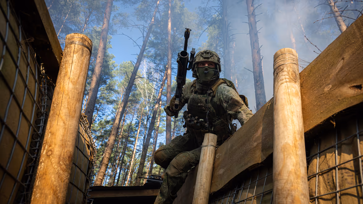 Militairen in loopgraven met geweren en helmen op.