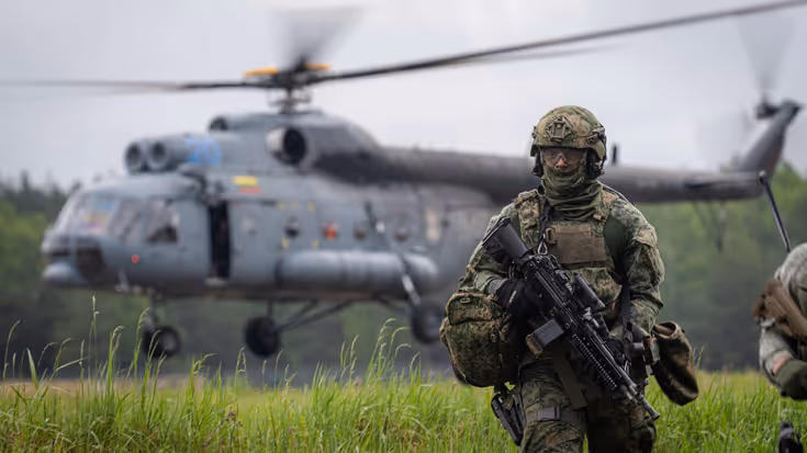 Helikopter met draaiende rotorbladen. Op voorgrond militair.