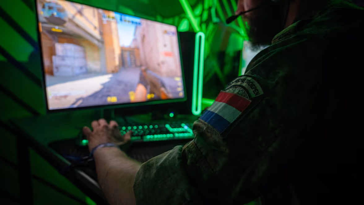 Een militair toont zijn geweer aan een burger. Een militair speelt een videogame.