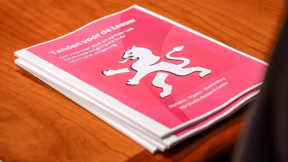 Stapeltje rapporten met rode kaft en afbeelding witte leeuw op houten tafel.