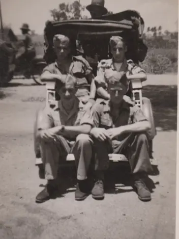 Oude foto met 4 militairen zittend op de achterkant van een auto.
