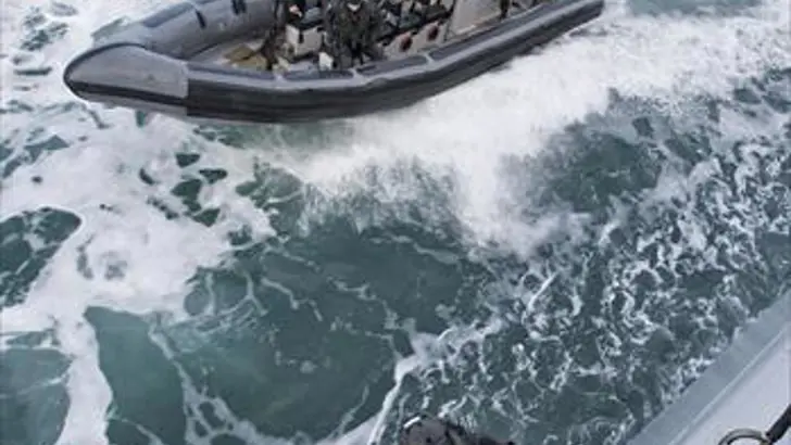 Een boardingteam in een RHIB komt aanvaren bij een schip.