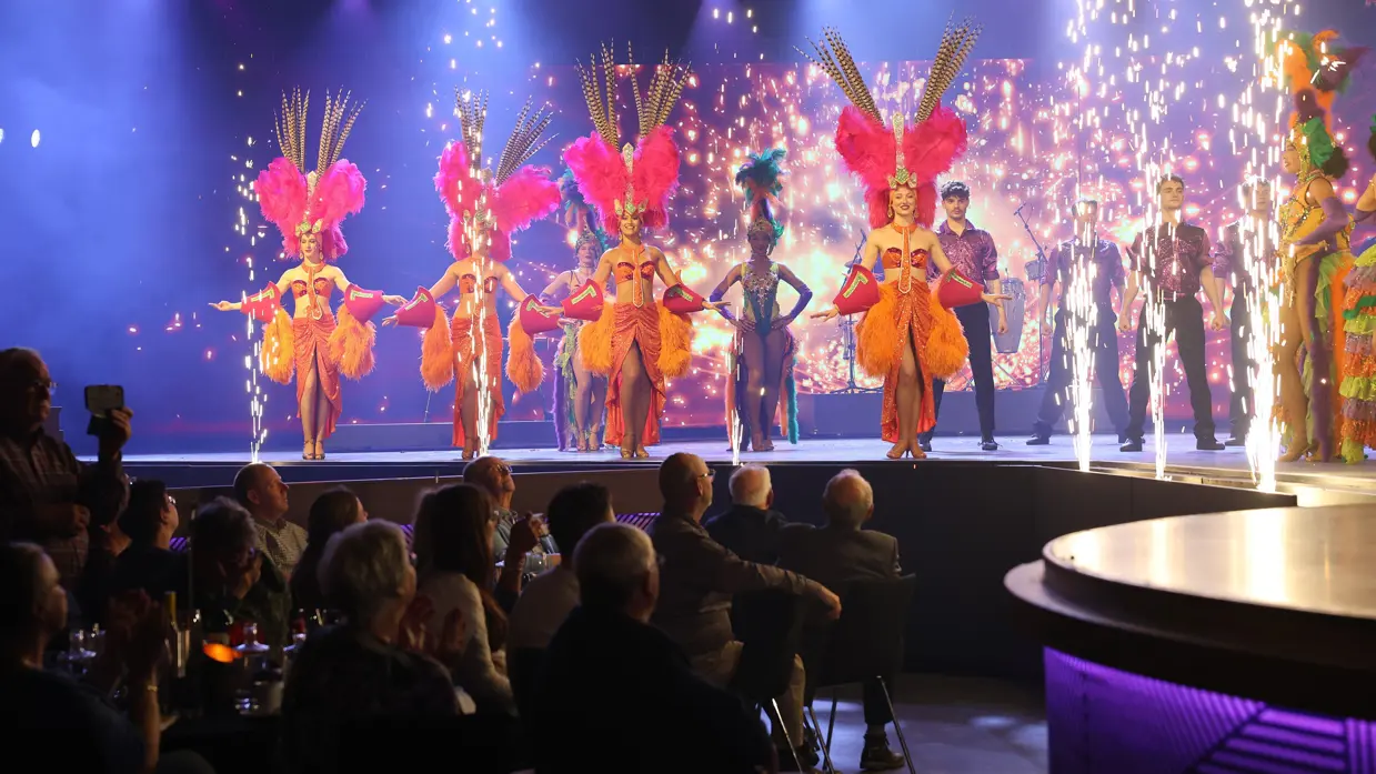 Danseressen, dansers en vuurwerk op een podium voor publiek.