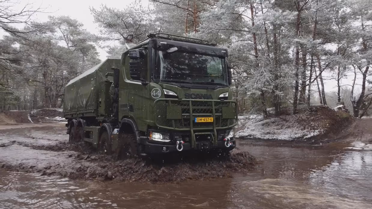 Een truck rijdt door sneeuw en modder, in een grote plas.