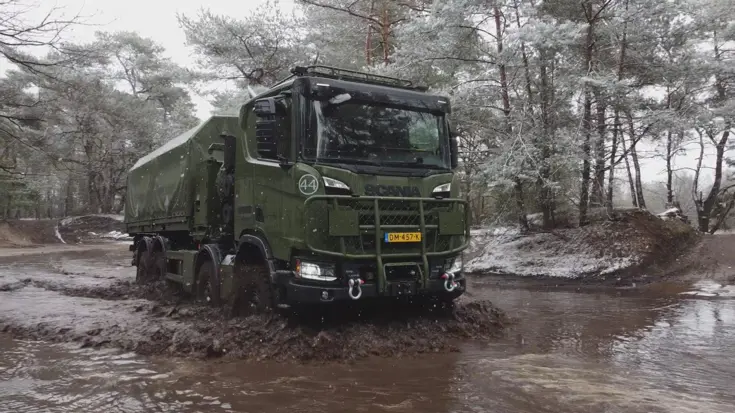 Een 8-wielaangedreven Scania Gryphus high operational rijdt door een diepe modderpoel op een oefenterrein.