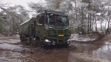 Een truck rijdt door sneeuw en modder, in een grote plas.