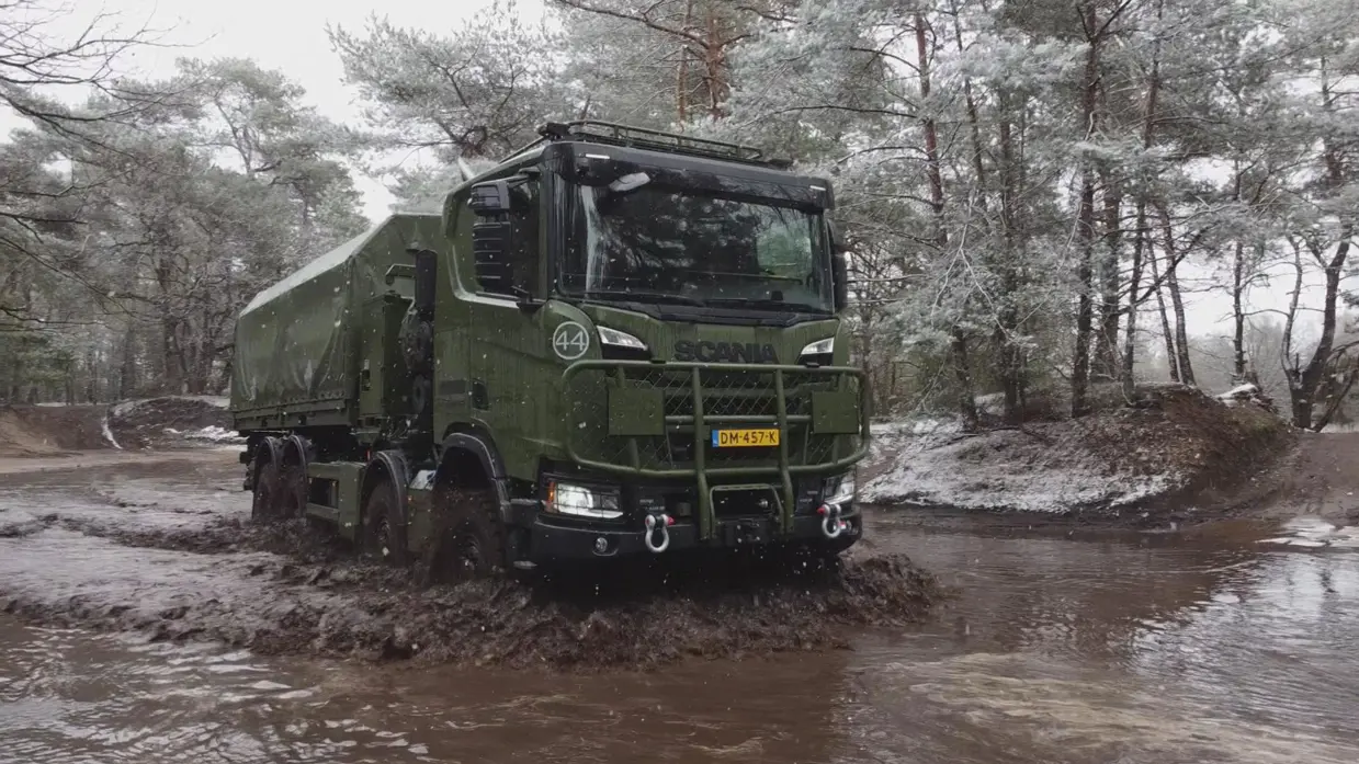 Een 8-wielaangedreven Scania Gryphus high operational rijdt door een diepe modderpoel op een oefenterrein.