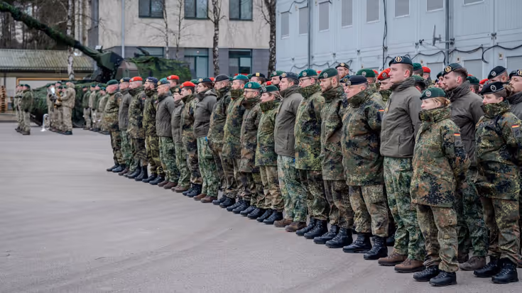 Groep militairen in de houding op binnenplaats. Een tank staat op de achtergrond.
