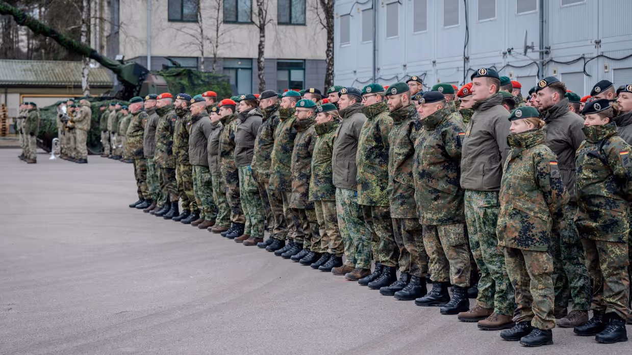 Groep militairen in de houding op binnenplaats. Een tank staat op de achtergrond.