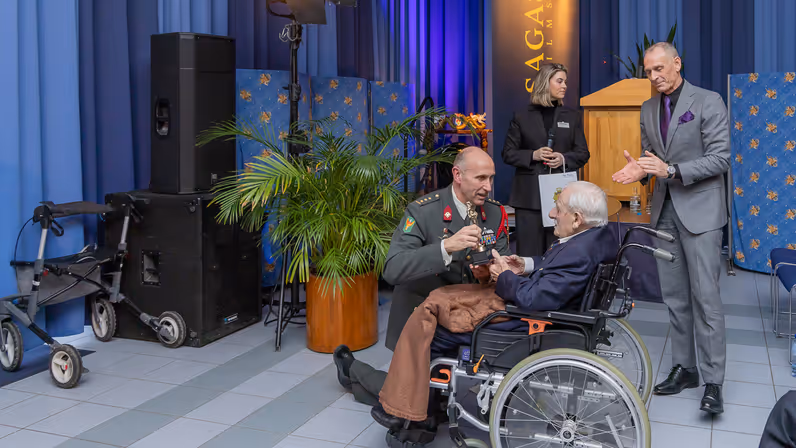 Alttekst = Veteraan Ton Hazeleger ontvangt een Oscarbeeld uit handen van de commandant van Bronbeek. 