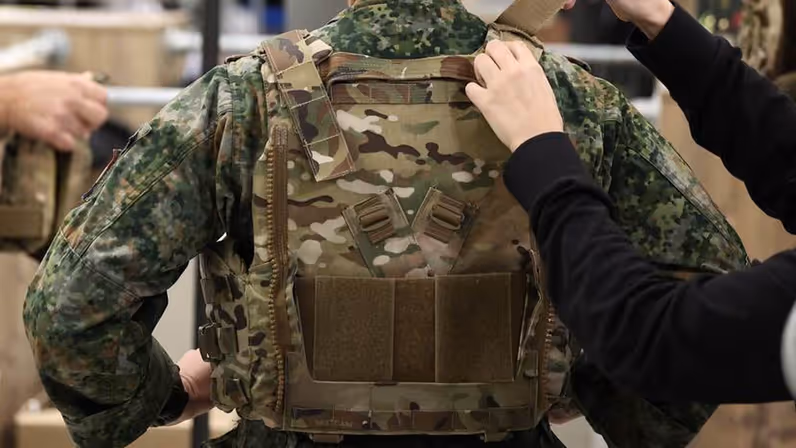 Handen stellen een scherfvest af bij een vrouw van wie alleen de rug zichtbaar is.