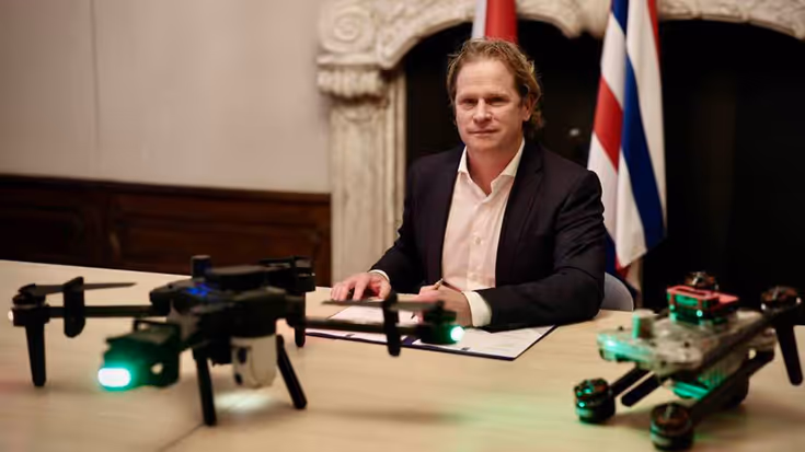 Staatssecretaris Tuinman zit achter de tafel waar 2 drones op staan.