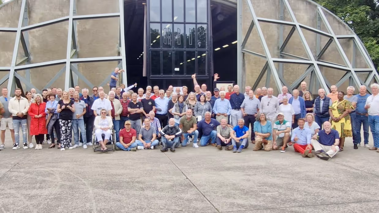 Een groep mensen poseert voor een ronde vliegtuigshelter.