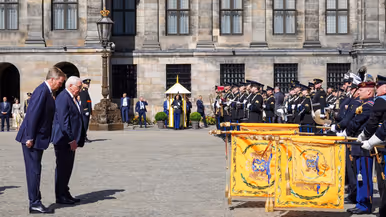 Koning Willem-Alexander en de bondspresident van Duitsland, Frank-Walter Steinmeier, buigen voor in rijen opgestelde militairen gekleed in ceremonieel tenue. Drie van hen steken oranje vaandels naar hen uit.