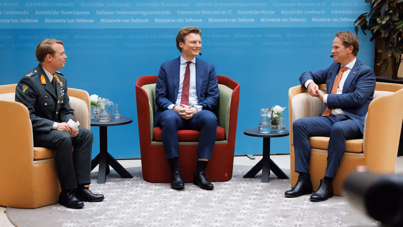 Brekelmans en Tuinman zitten in gele stoelen terwijl ze worden geïnterviewd door een militair 