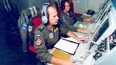  Twee militairen achter radarschermen in een vliegtuig.