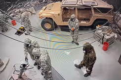 5 militairen met gasmaskers in een ruimte met een voertuig.