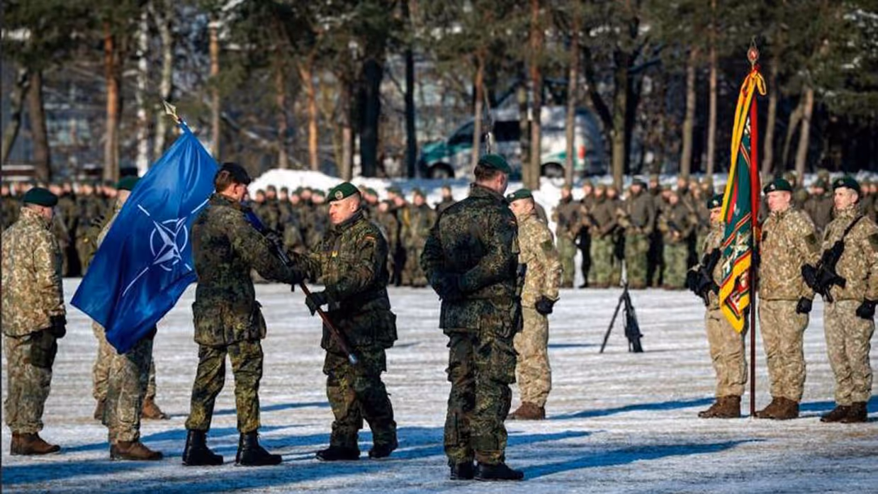 Militairen op witte, besneeuwde ondergrond met NAVO-vlag in de hand van 1 van hen.