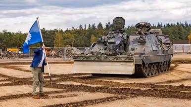 Gijs Tuinman plant een vlag in de grond op de plek waar het TCL gebouwd wordt.   +Een Kodiak is aan het graven. 