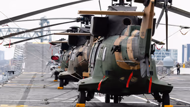 Twee oorlogsschepen liggen in een haven en op een groot schip staan helikopters opgesteld.