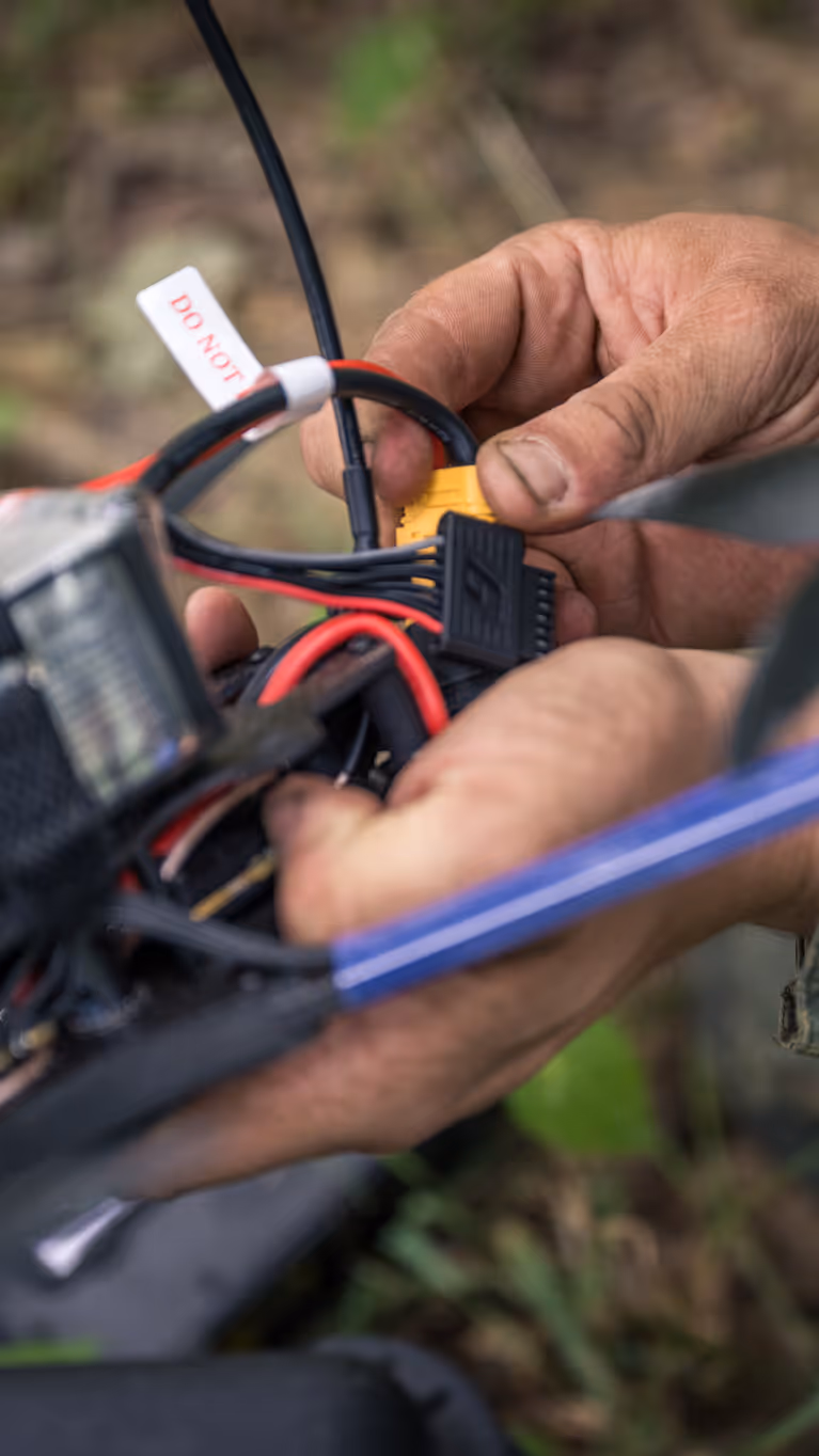 Een drone-operator zit met zijn handen aan een drone. 
