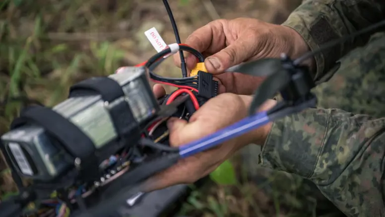 Een drone-operator zit met zijn handen aan een drone. 